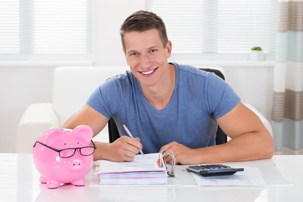 Man With Piggybank Calculating Receipt