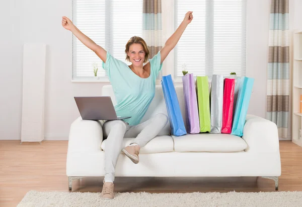 Woman On Sofa With Laptop And Shopping Bags