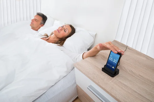 Woman On Bed Snoozing Alarm Clock