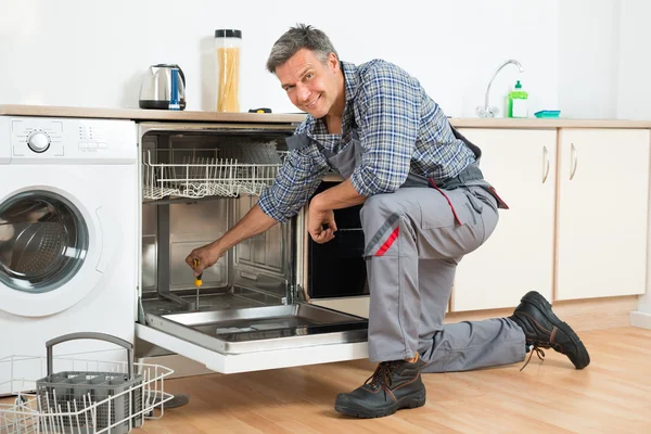 Repairman Repairing Dishwasher With Screwdriver In Kitchen