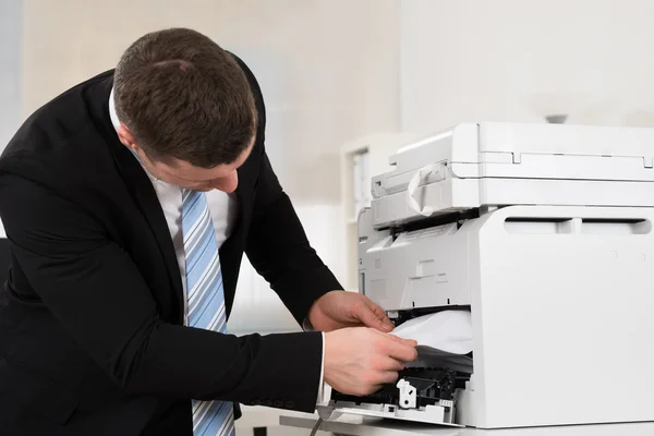Businessman Removing Paper Stuck In Printer