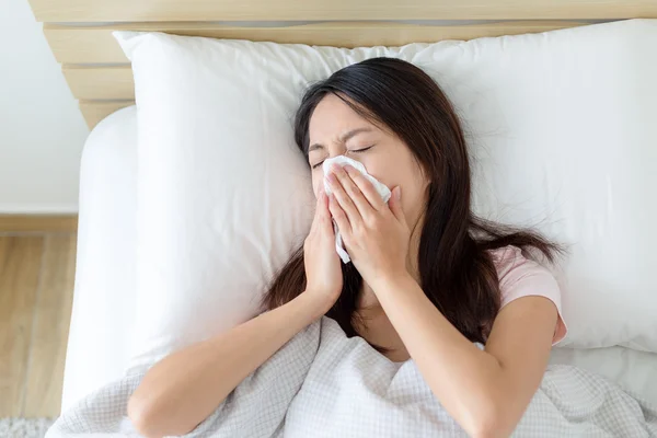 Woman getting cold and sneezing on bed