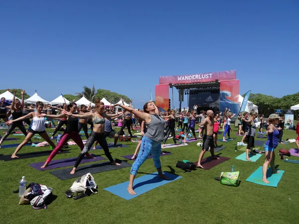 People raise arms wide and spread legs during outdoor yoga class