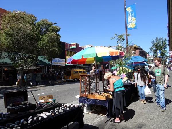 People shopping at street booths on sidewalk surrounded by store