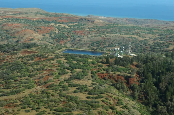 Aerial of countryside running to the ocean with Water reservoir and communications towers on Molokai