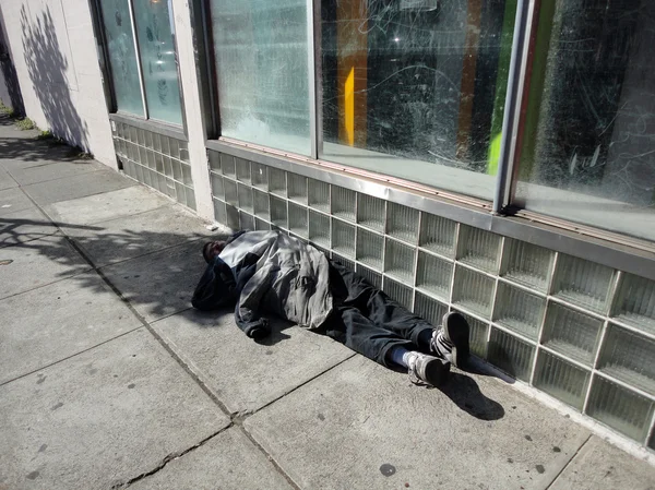 Bundled up homeless person sleep along side of building in the m
