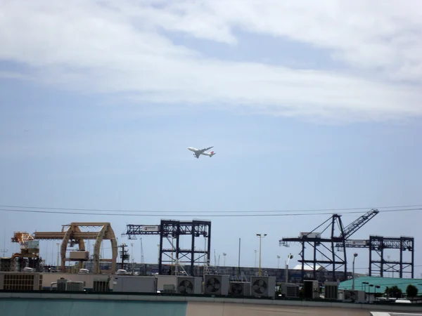 Airplane flies above shipping cranes