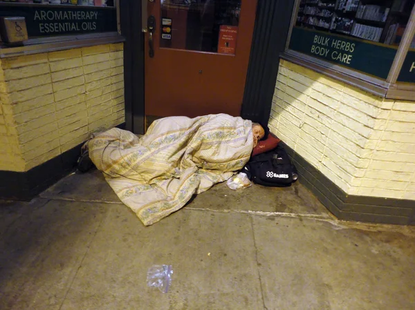 Bundled up homeless person sleep in door way of store under a bl