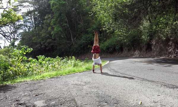 Man Handstands along curvy Mountain road with lush vegetation