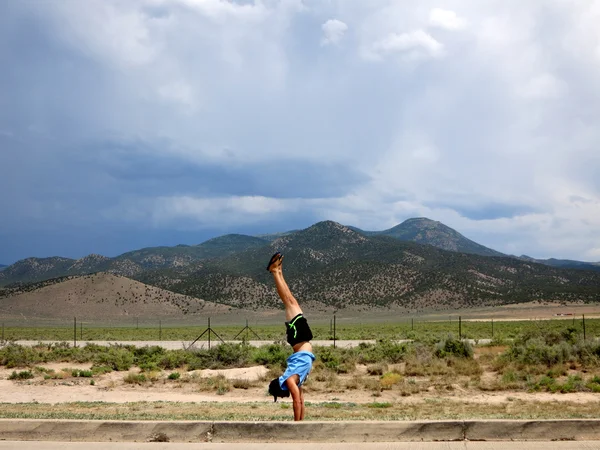 Man wearing a hat, t-shirt, shorts, and slippers does Handstands