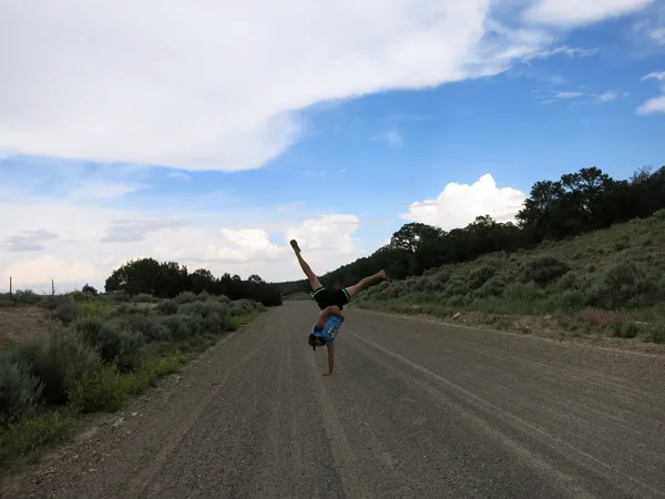 Man does one handed Handstands on long straight dirt road