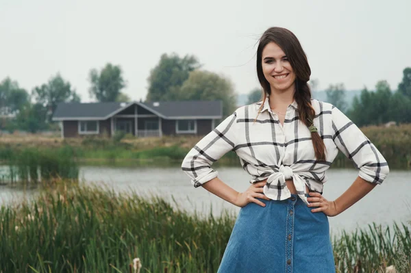 Playful country lady posing against pond and house on ranch