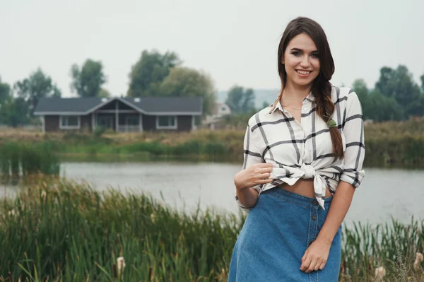 Playful country lady posing against pond and house on ranch