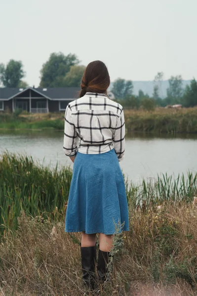Country lady standing against pond on ranch back to viewer