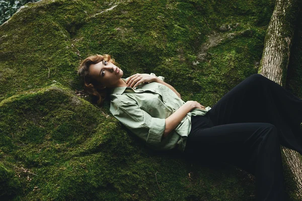 Pretty blonde posing on moss dressed in masculine shirt and stylish trousers.