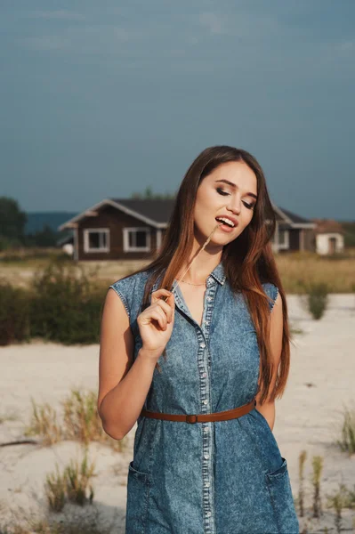 Brown haired rural lady standing on sand against ranch house