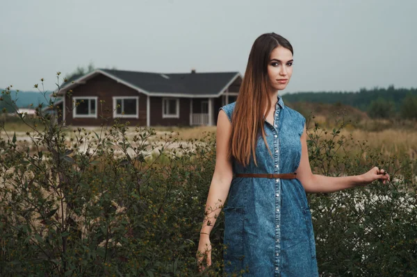Cute countryside lady standing in tall grass against ranch house