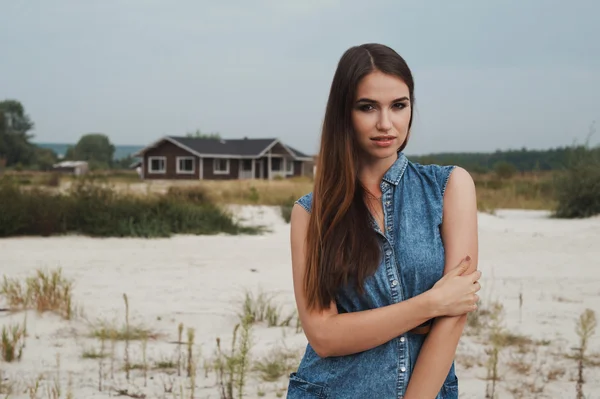 Brown haired rural lady standing on sand against ranch house