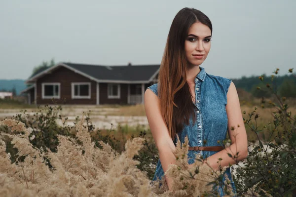 Cute countryside lady standing in tall grass against ranch house