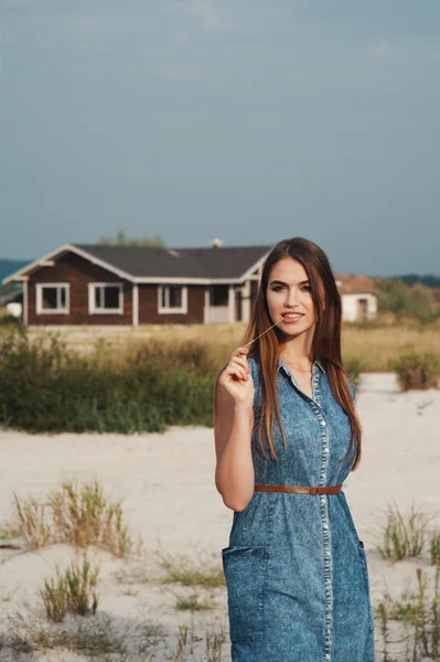Brown haired rural lady standing on sand against ranch house
