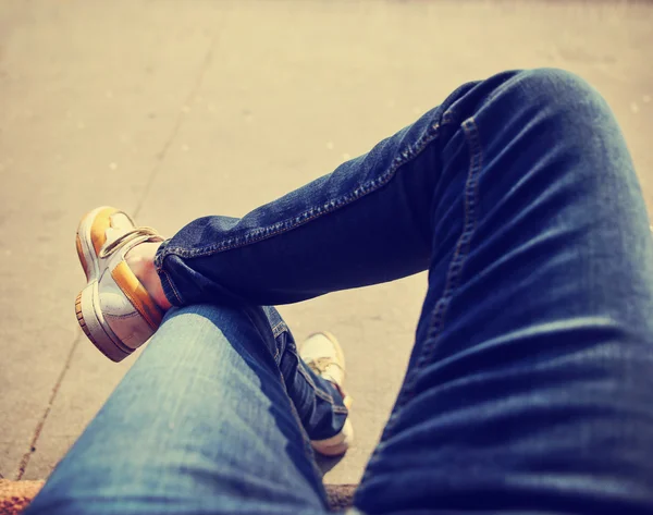 A hipster sitting downtown with crossed legs on a sidewalk bench