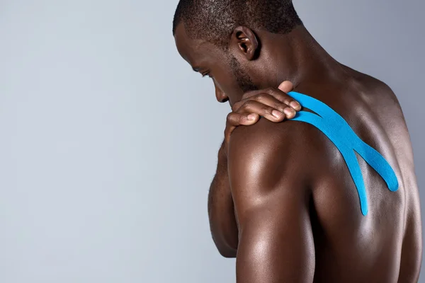African man touching his taped injured shoulder, sports injury painful