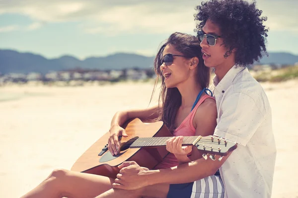 Hispanic couple playing guitar on beach