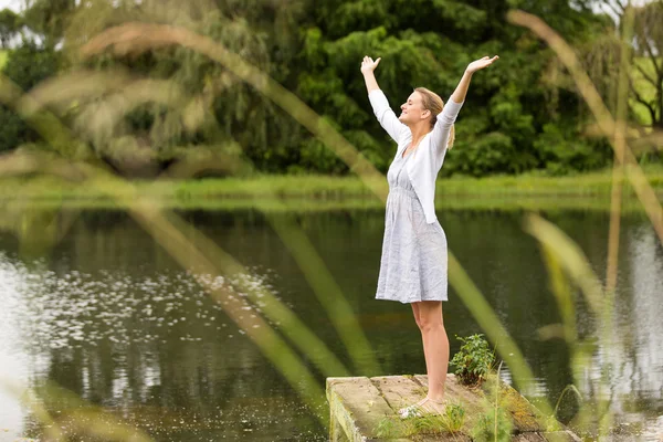 Young woman with arms outstretched by the lake