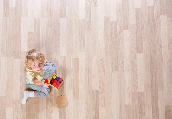 Little blond kid boy playing with colorful building blocks on floor top view