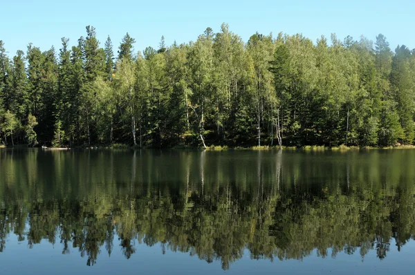In the clear water of a forest lake reflects the sky, mountain, forest and clouds. Photo partially tinted.