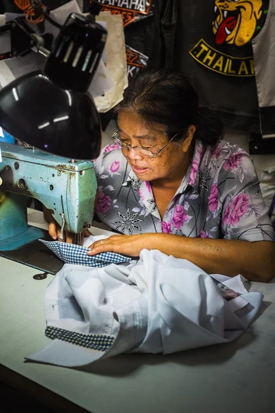 Old woman sews on sewing machine
