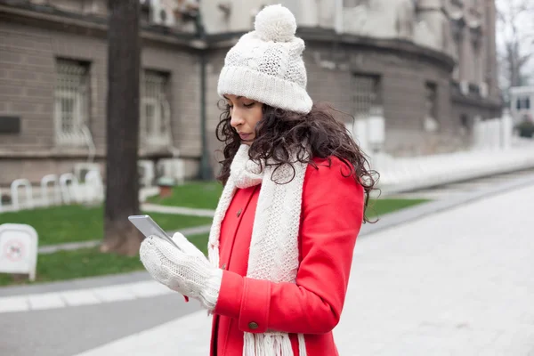 Beautiful woman in red coat and wool cap and gloves with smartph