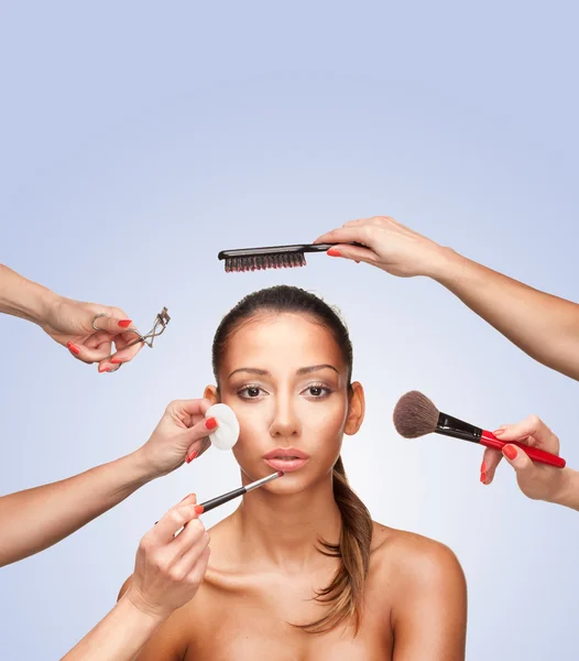 Portrait of young female surrounded by hands with beauty tools