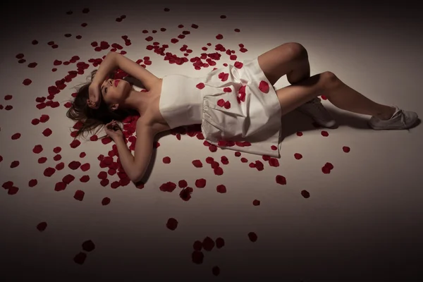 Beauty brunette woman wearing white dress and rose petals