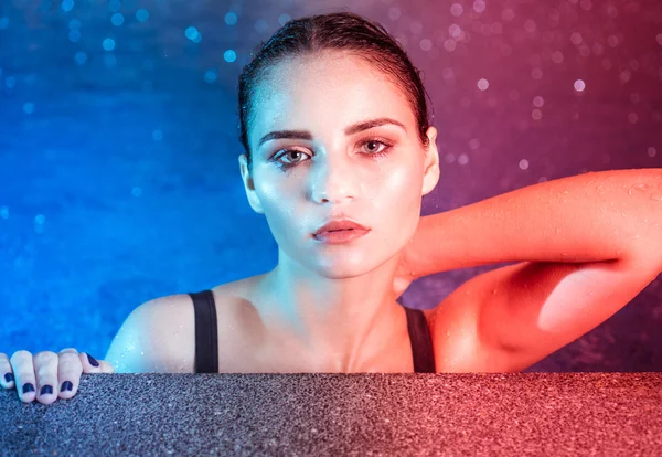 Closeup portrait of young woman beauty in pool during rainy evening with wet makeup looking into the camera