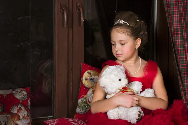 Thoughtful Girl in a red dress hugging a plush bear