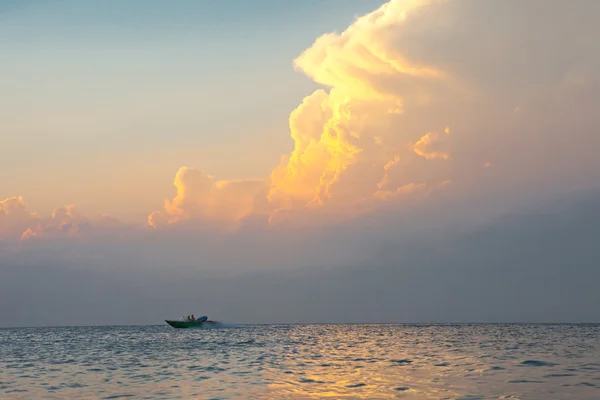 Powerboat on the horizon against the evening sea landscape with huge pink clouds.