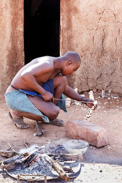 Himba man adjusts wooden souvenirs in fireplace for tourists