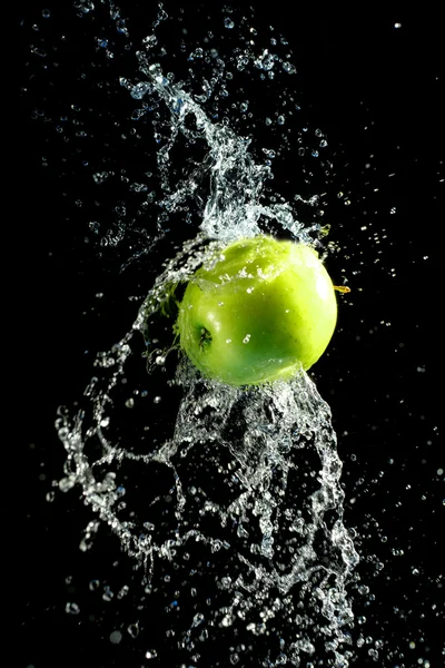 Green apple with water splash, on black