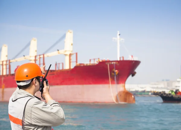 Harbor dock worker talking on radio with ship background