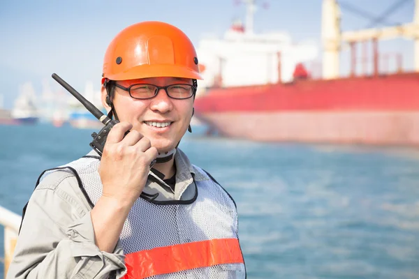 Smiling dock worker tholding radio and ship background