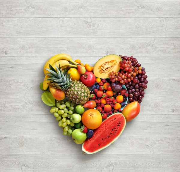 Food photography of heart made from different fruits on white wooden table.