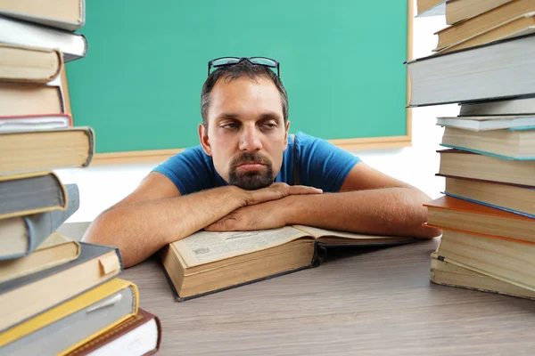 Teacher resting his chin on his hands, laying on a table with opened book.