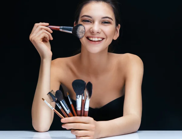 Smiling brunette girl with brushes for make up on black background.