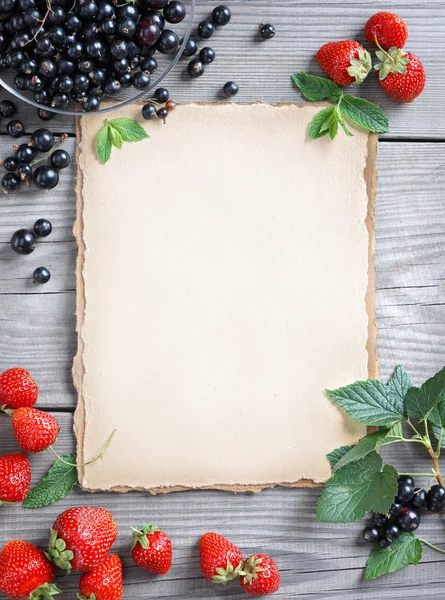 Healthy food background. Old paper with strawberry and currant on wooden table