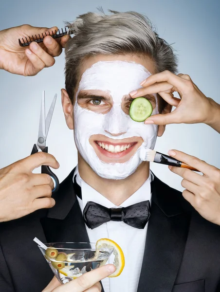 Happy elegant man with moisturizing facial mask surrounded by the multifunctional service  (stylist, beautician, hairdresser)