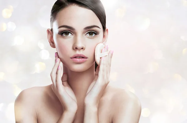 Young woman applying blusher on her face with powder puff, skin care concept