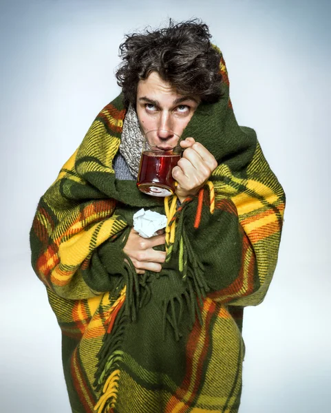 Ill Man covered with plaid blanket with hot tea