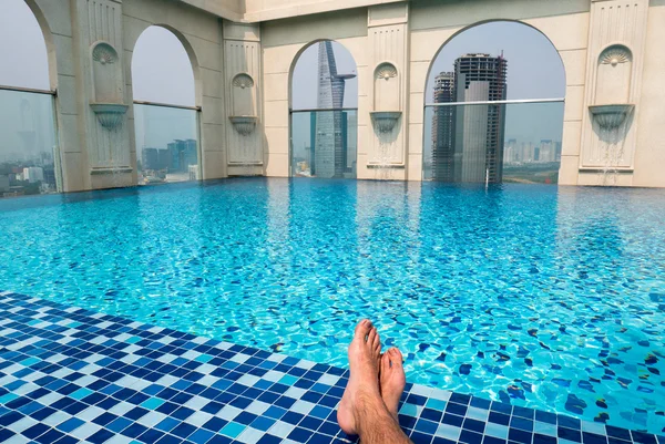 Feet over the sparkling pool on top of building with Saigon aeri