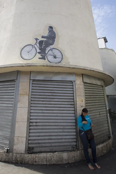 Woman waiting with a drawing of Hugo Chavez on a bike on top. Ca